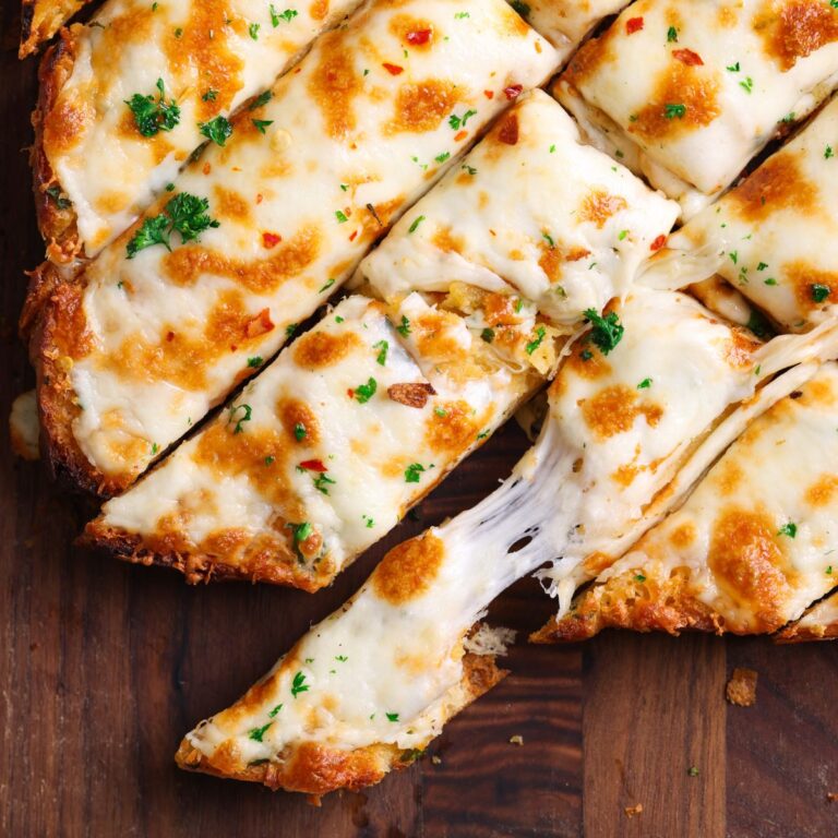 cheesy garlic bread sticks on a wooden cutting board with broiled melted cheese and chopped parsley on top. one stick is broken into half with cheese stretching between both halves