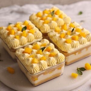 4 dessert cups containing mango tiramisu decorated with cream dollops and fresh mango