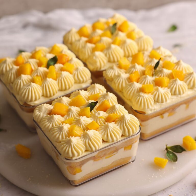 4 dessert cups containing mango tiramisu decorated with cream dollops and fresh mango