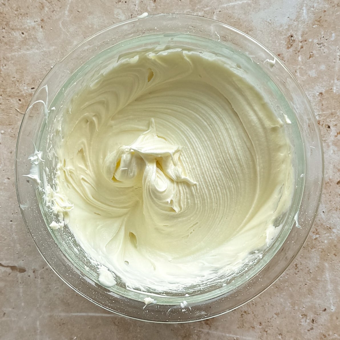 A glass bowl filled with smooth, creamy, whipped frosting or batter