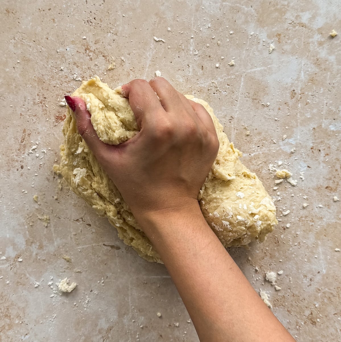 A hand kneads a ball of dough on a lightly floured surface