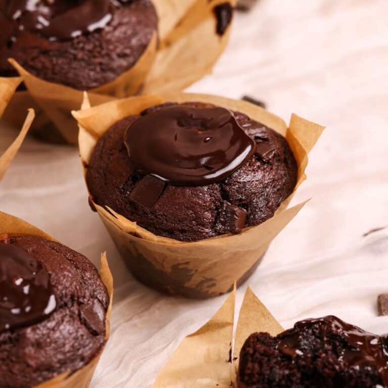 angled picture of a jumbo chocolate muffin with ganache on top; more seen in the background