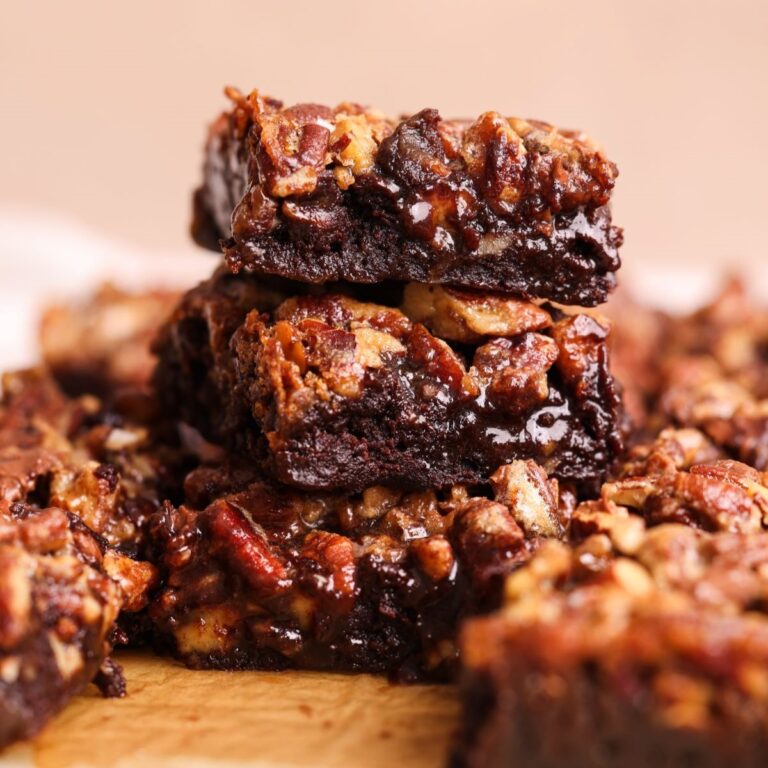 3 pecan pie brownies stacked on top of each other with more on the side. brownies have a layer of fudgy gooey brownie topped with a pecan pie filling