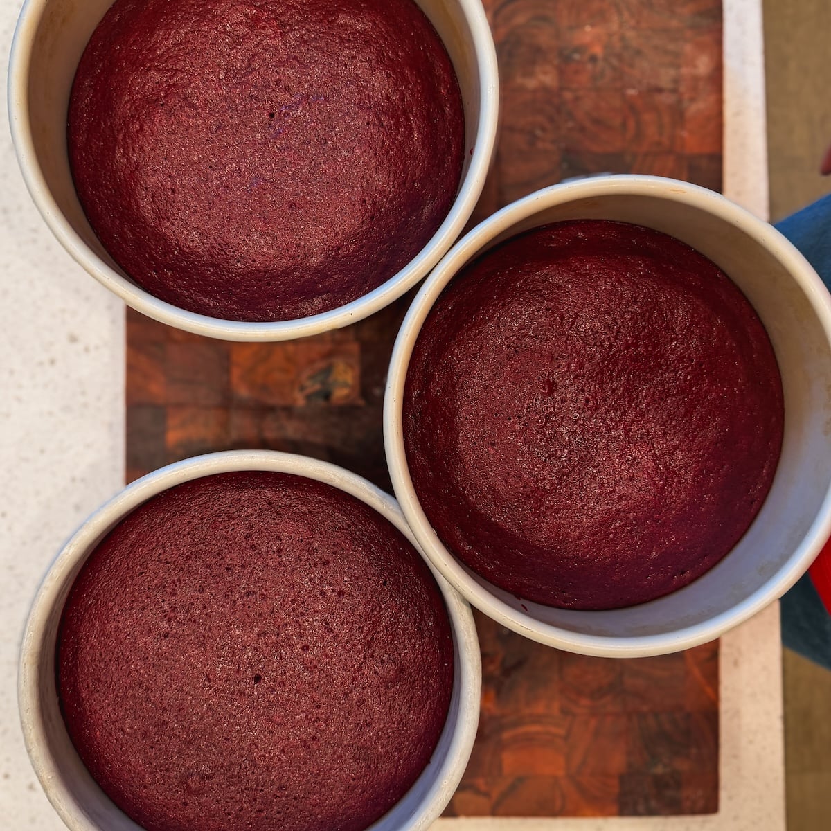 Three round cake pans filled with freshly baked red velvet cakes, arranged close together on a wooden surface