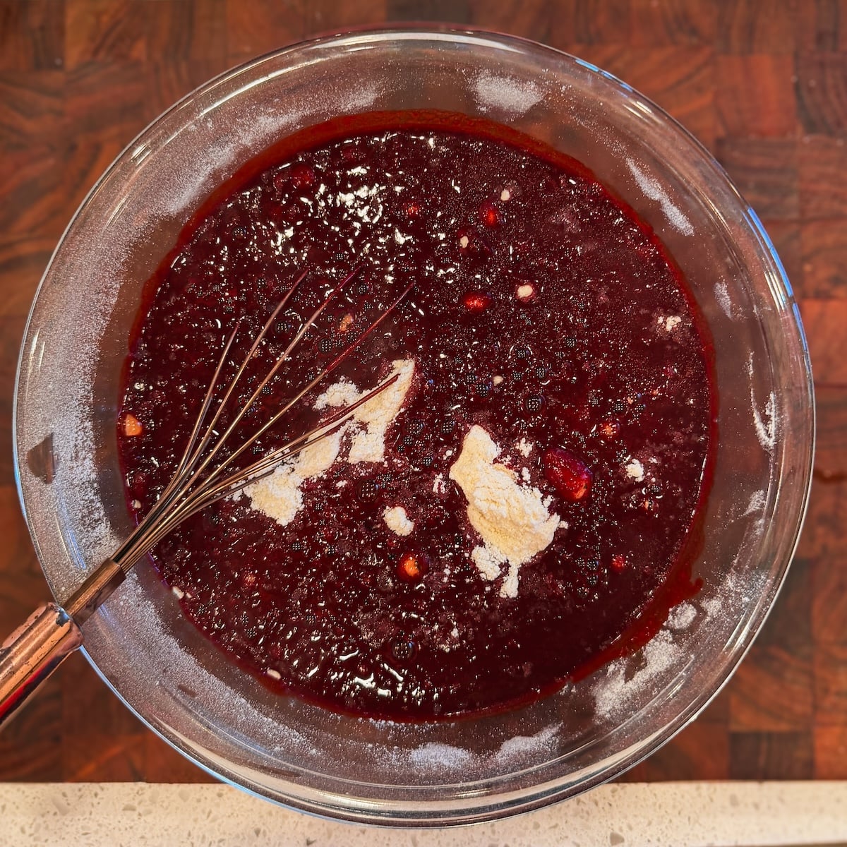 A glass bowl filled with a red liquids being mixed into dry ingredients for red velvet cake