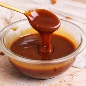 deep golden salted caramel sauce in a glass bowl with a spoon lifting and pouring in some sauce in a ribbon; close up