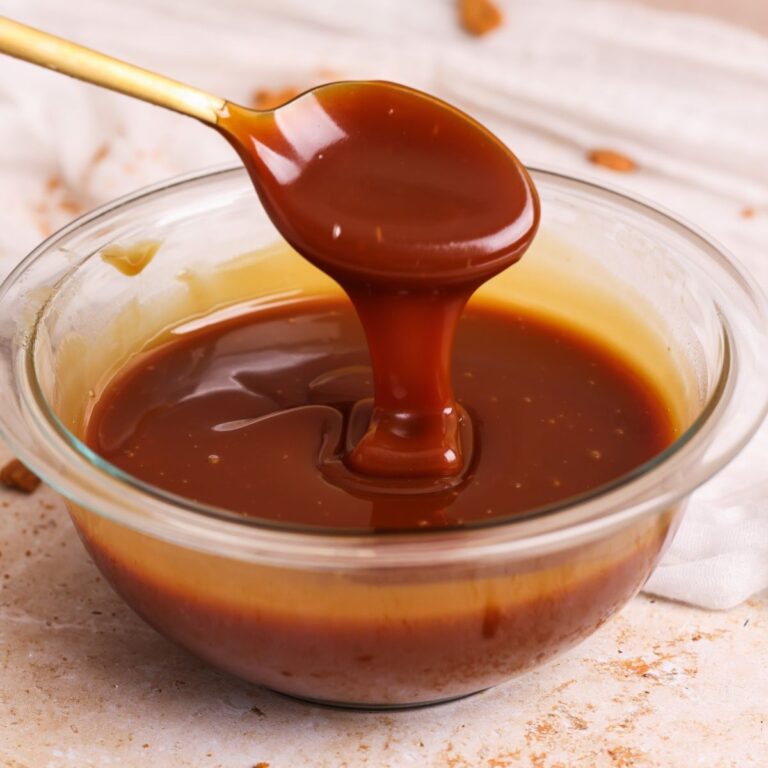 deep golden salted caramel sauce in a glass bowl with a spoon lifting and pouring in some sauce in a ribbon; close up