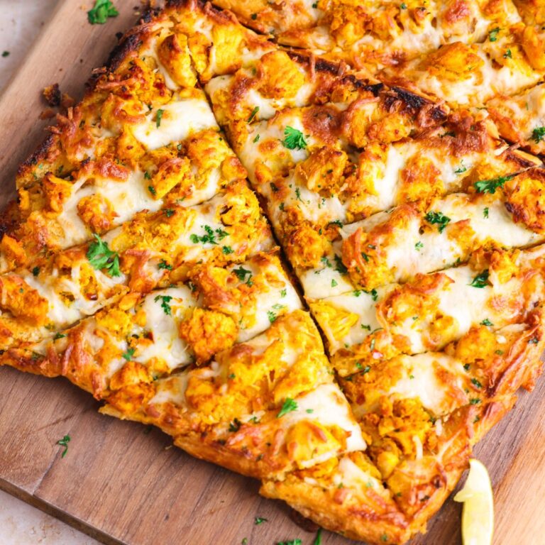 tandoori chicken garlic bread on a wooden board cut into slices. bread is crispy and golden with lots of tandoori chicken and cheese on top.