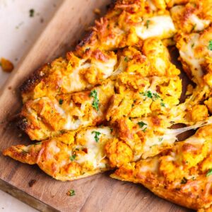 Close up of three tandoori chicken garlic bread sliders that are being pulled apart from the bread with a cheese pull