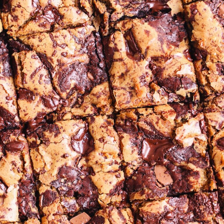close up of a batch of brown butter brookies from the top which have been cut into squares. they have a shiny surface with a mixture of cookie dough and brownie batter