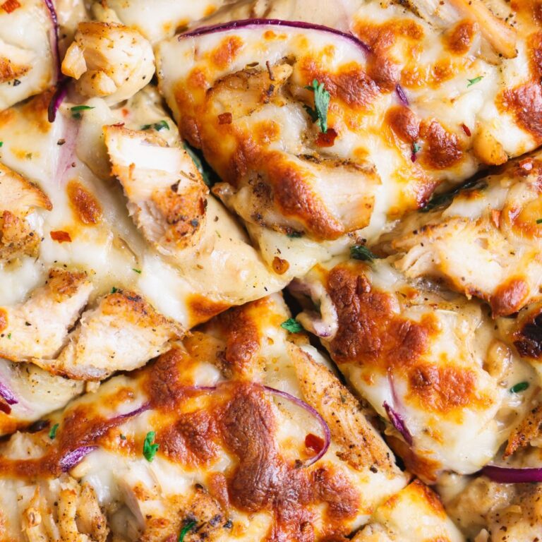 close up of sliced chicken alfredo flatbread from the top. the bread has lots of alfredo sauce, grilled chicken, and melted charred cheese