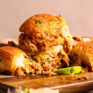 chicken birria sliders stacked on top of each other imaged from the side. the sliders are stuffed with shredded chicken birria, sauce and cheese, and dipped in more sauce