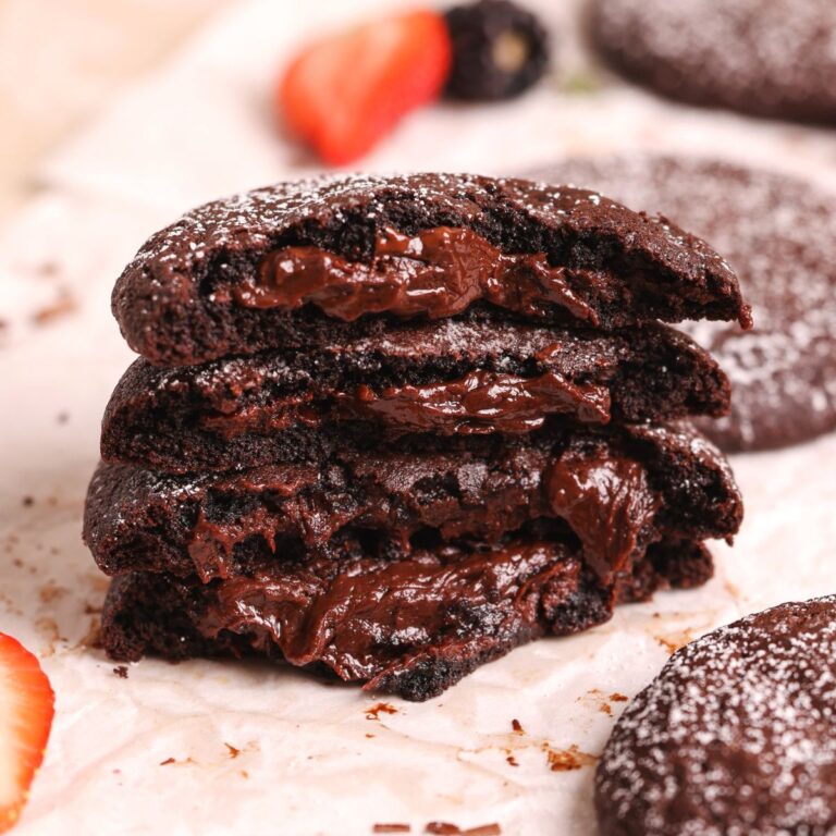 stack of 4 molten lava cookies broken into half to show the soft, chewy texture and fudge filled interior. more seen in the background