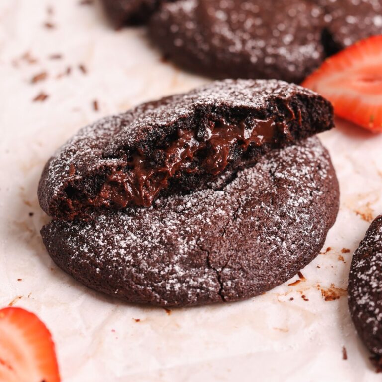close up of a molten lava cookie broken into half with one half resting on top of the other. the cookie looks very gooey and fudgy and has fudge oozing out from the middle.