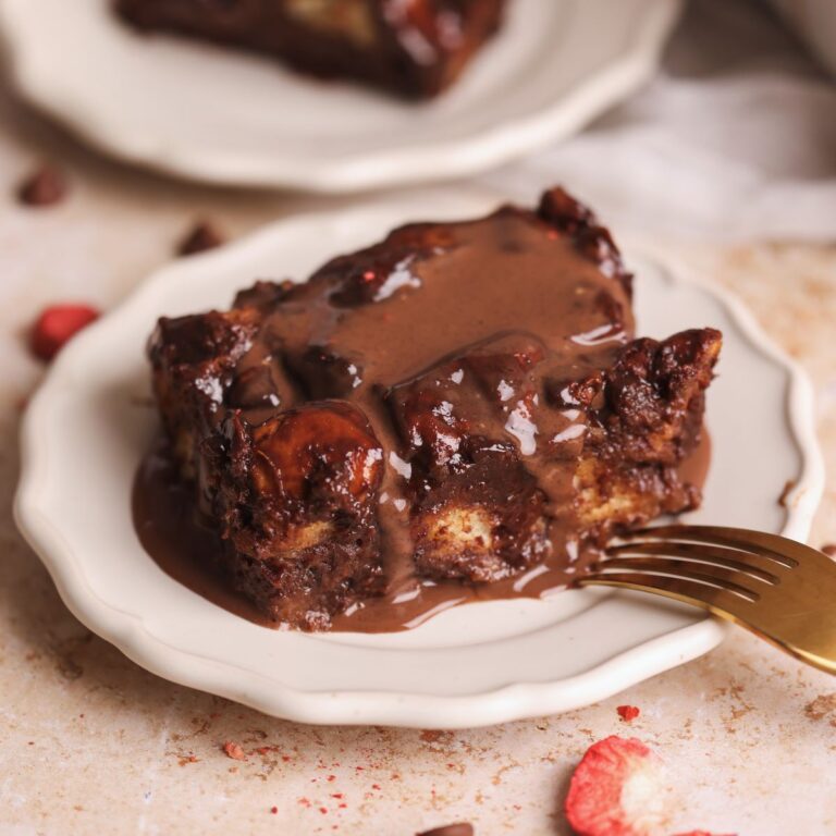 slice of chocolate bread pudding on a small plate with chocolate creme anglaise poured on top, fork resting on the side