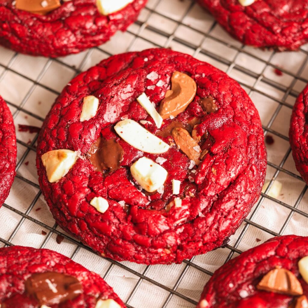 close up of a red velvet chocolate chip cookie with chocolate chunks on it and more cookies seen surrounding it
