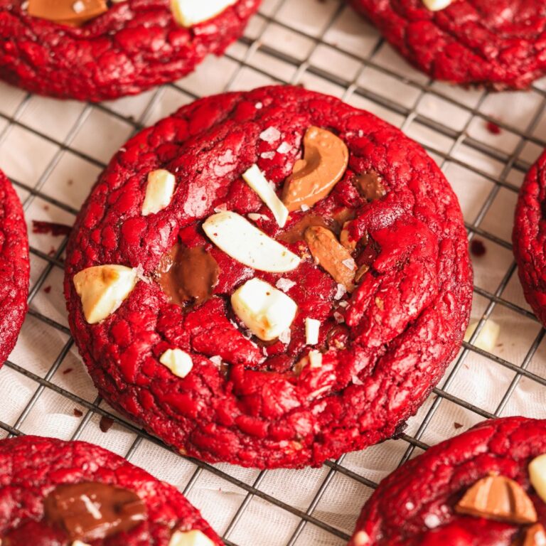 close up of a red velvet chocolate chip cookie with chocolate chunks on it and more cookies seen surrounding it