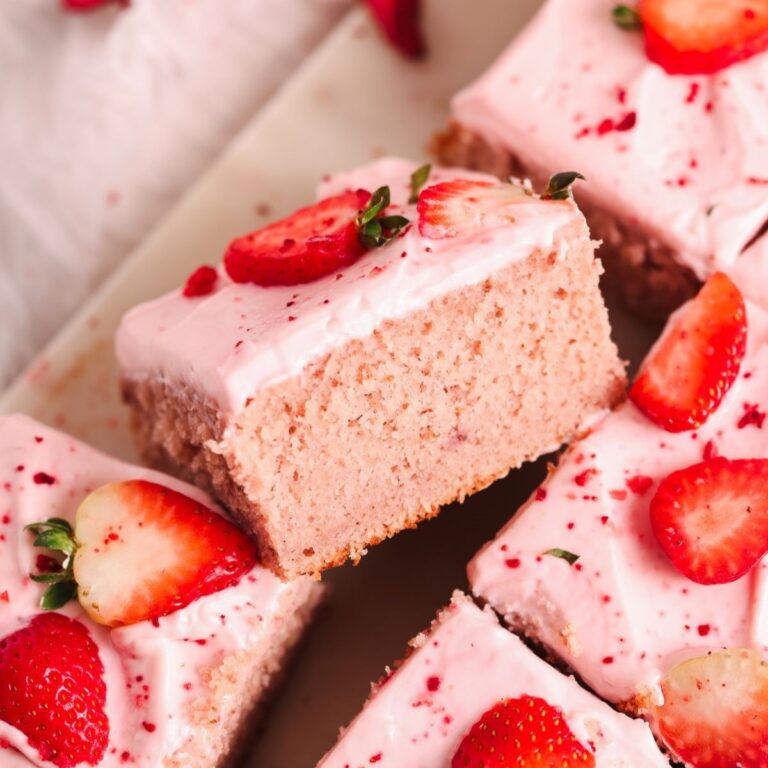 slice of strawberry sheet cake placed sideways next to other slices to show the soft fluffy texture of the cake