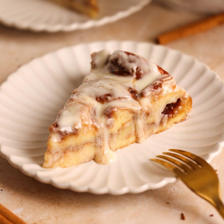 slice of cinnamon roll bread pudding on a small plate with a gooey interior, cinnamon sugar filling and dripping cream cheese icing on top
