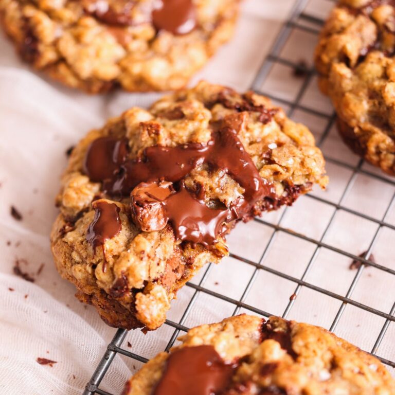 an oatmeal chocolate chip cookie with 2 bites taken out rest against a wire rack. it looks golden brown and crispy with lots of melted chocolate