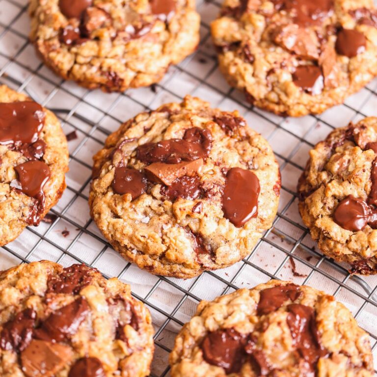 oatmeal chocolate chip cookies on a wire rack. cookies are golden brown and crispy outside with puddles of melted chocolate and flakey sea salt sprinkled on top. focus on one cookie