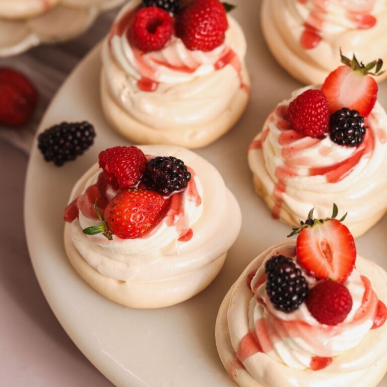 mini cheesecake pavlovas on a cake board. pavlovas have a cheesecake filling and are topped with a berry glaze and fresh berries