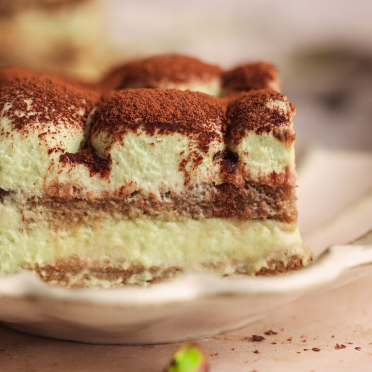close up from the side of a slice of pistachio tiramisu in a small plate with layers of ladyfingers and a pistachio mascarpone cream