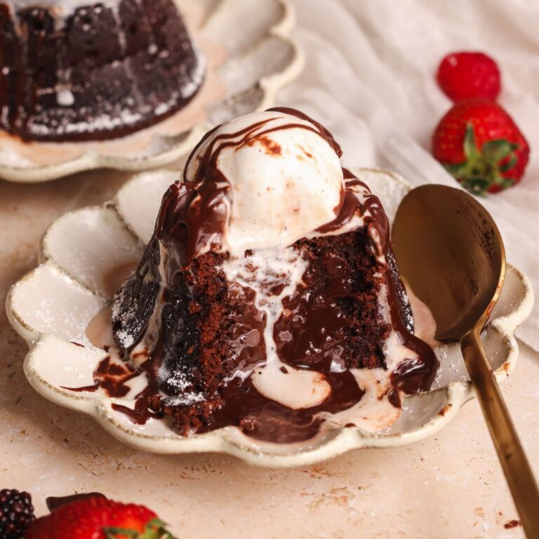 chocolate lava cake in a small plate with a scoop of vanilla ice cream. A bite has been removed to show the molten lava chocolate center. A spoon is resting with the cake on the side of the plate