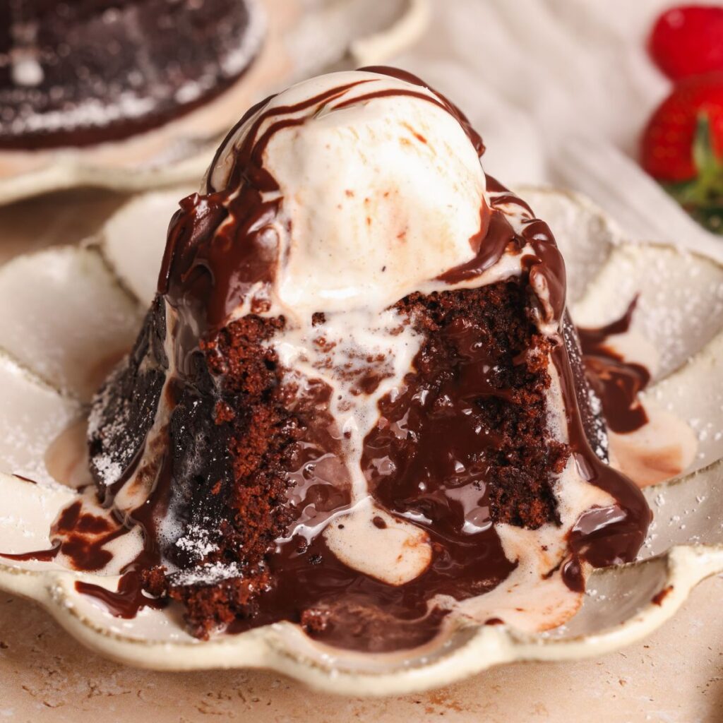 chocolate lava cake in a small plate with a scoop of vanilla ice cream. A bite has been removed to show the molten lava chocolate center