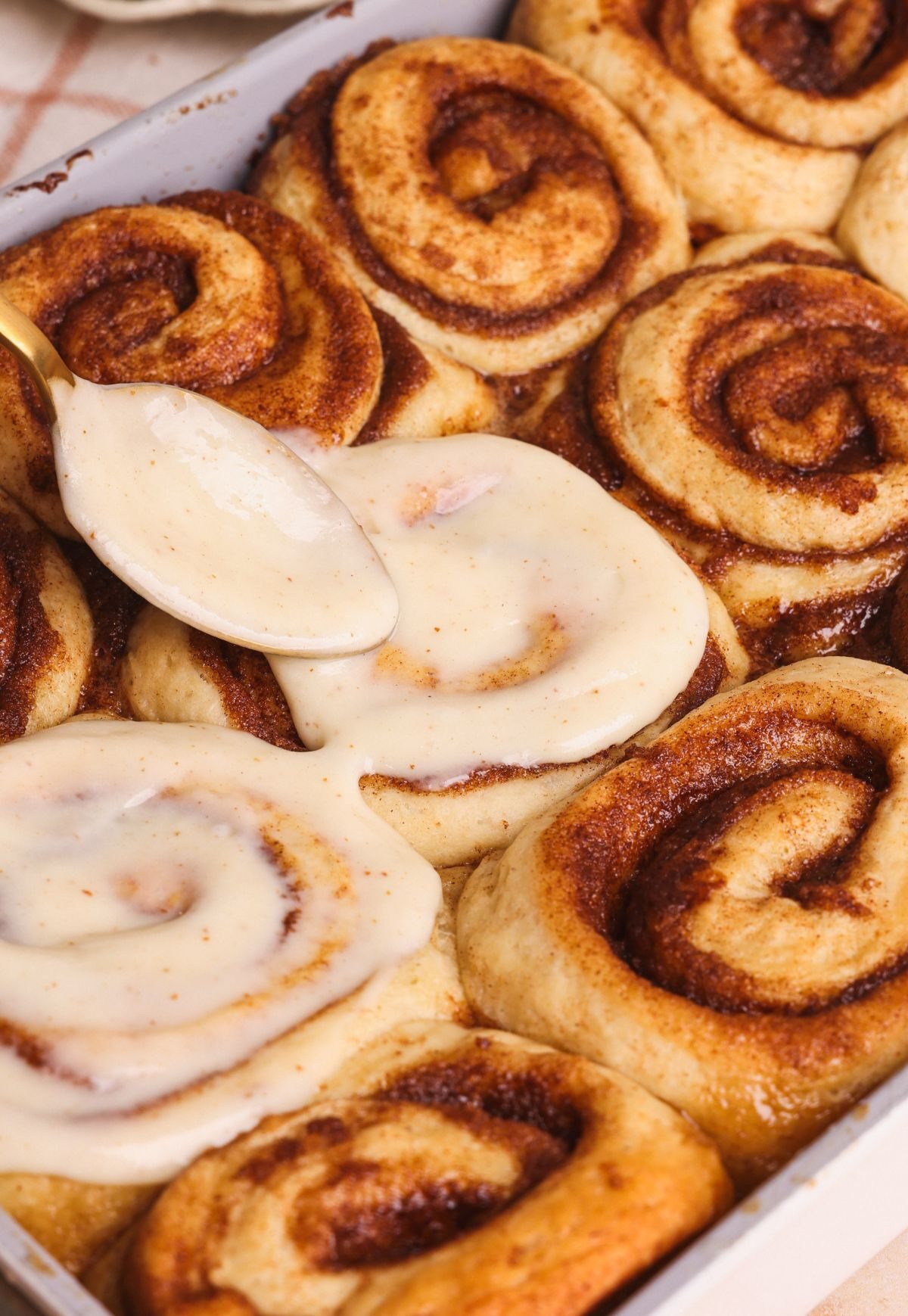 a spoon spreading cream cheese icing on a banana bread cinnamon roll