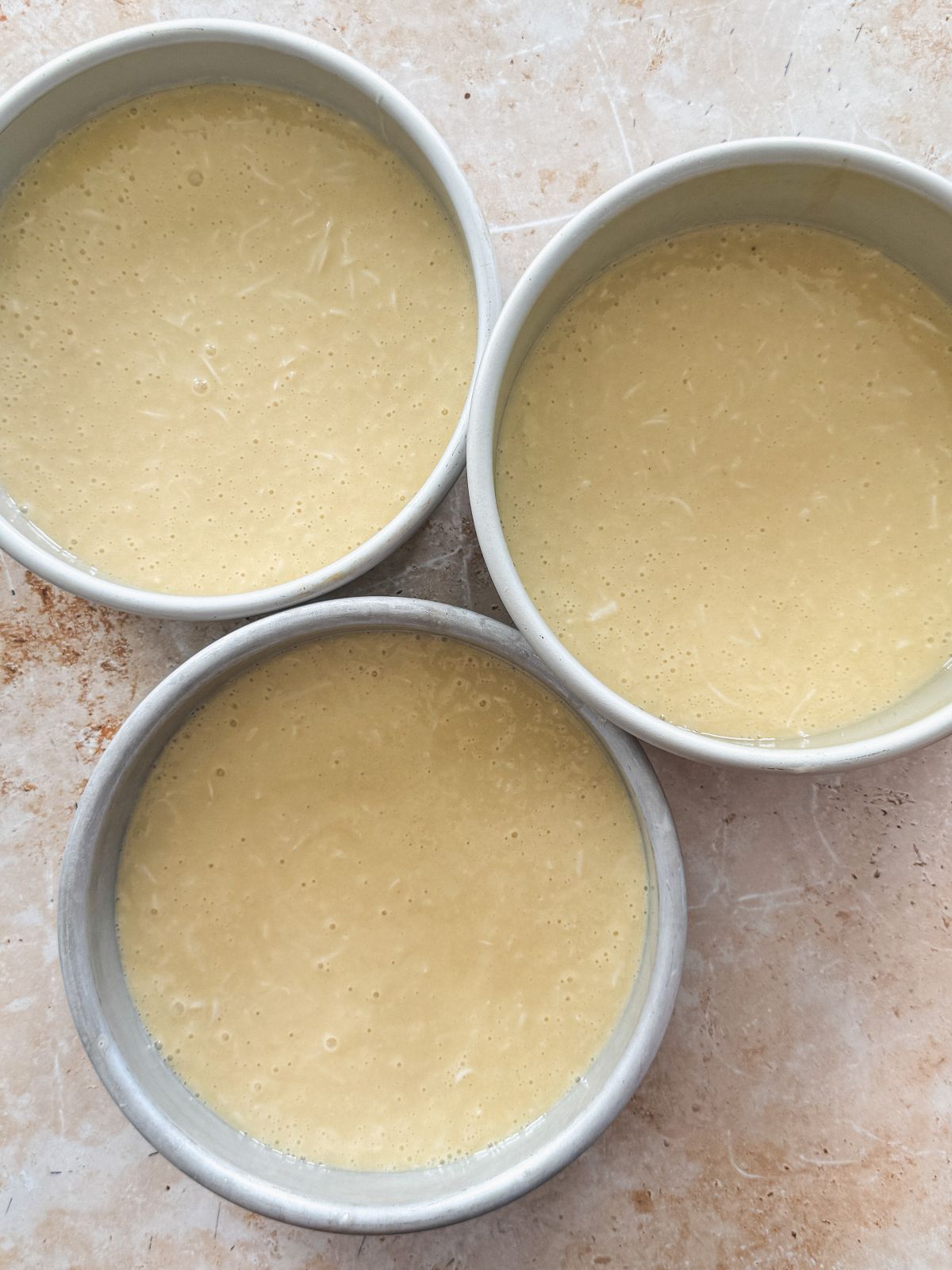 3 cake pans with coconut cake batter inside