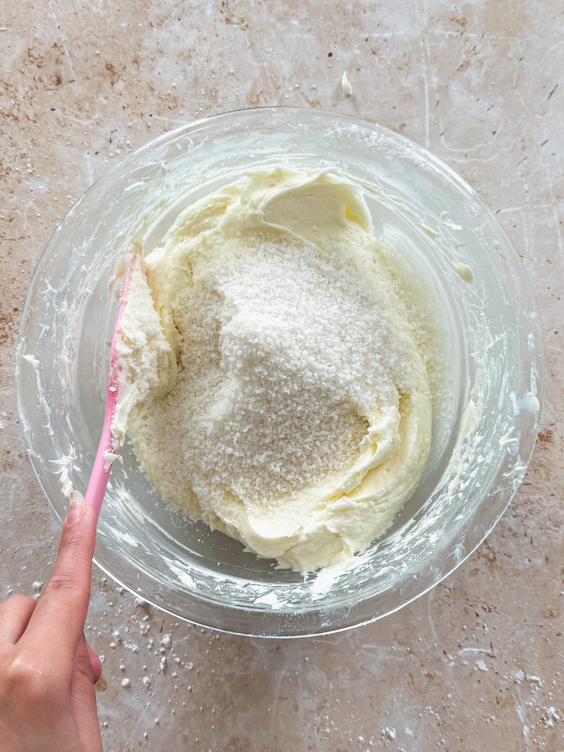 shredded coconut added to cream cheese frosting in a glass bowl