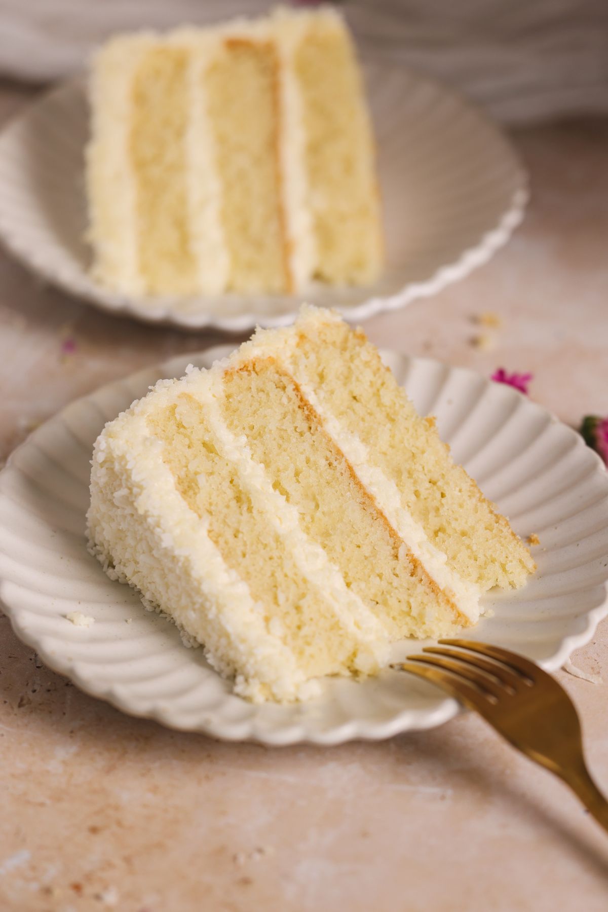 slice of coconut cake with 3 layers of cake and cream cheese frosting on a small plate with a fork resting on it