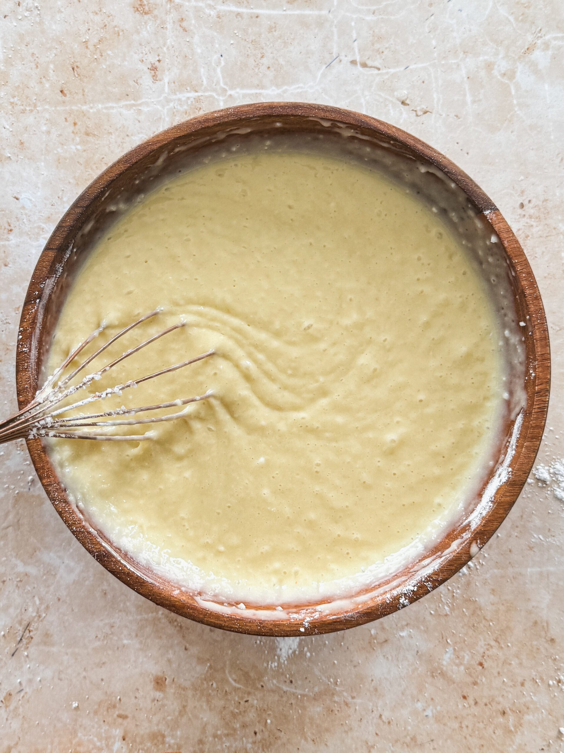 coconut cake batter with desiccated coconut in a wooden bowl with a whisk