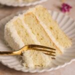 a fork taking out a bite from a slice of coconut cake on a small plate