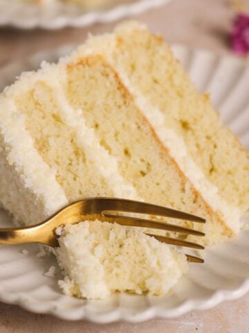 a fork taking out a bite from a slice of coconut cake on a small plate