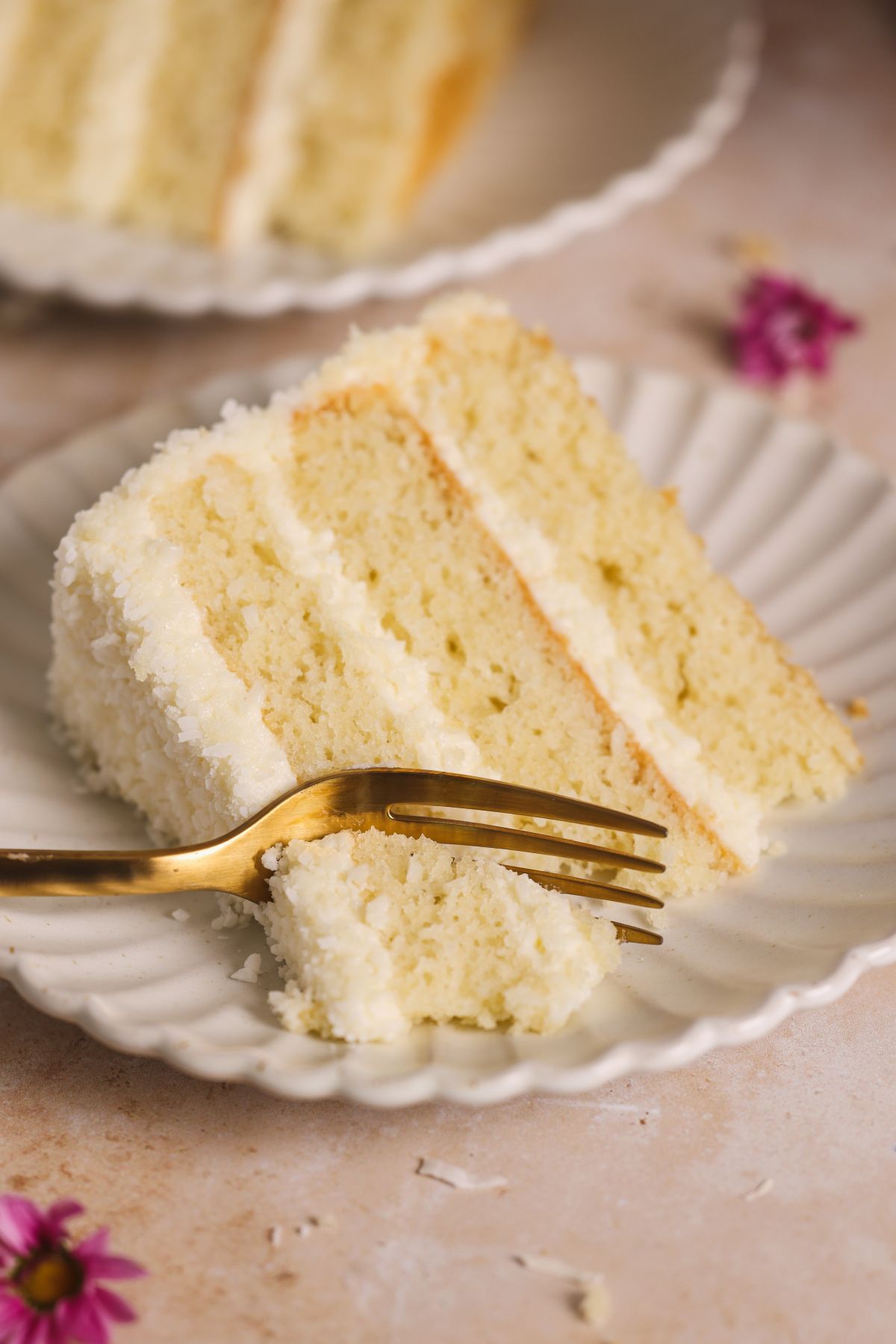 a fork taking out a bite from a slice of coconut cake on a small plate