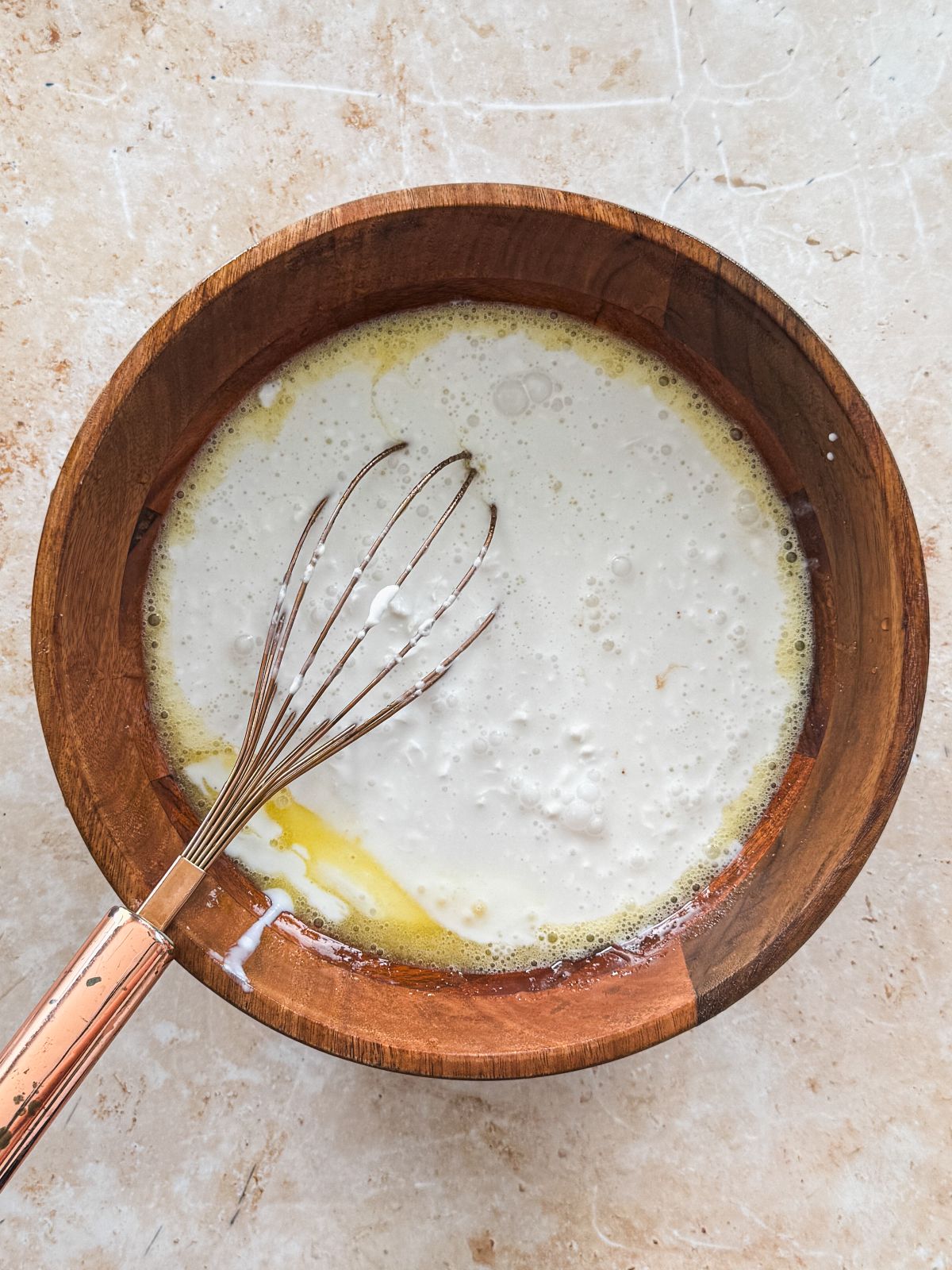 coconut milk added to wet ingredients in a wooden bowl with a whsik