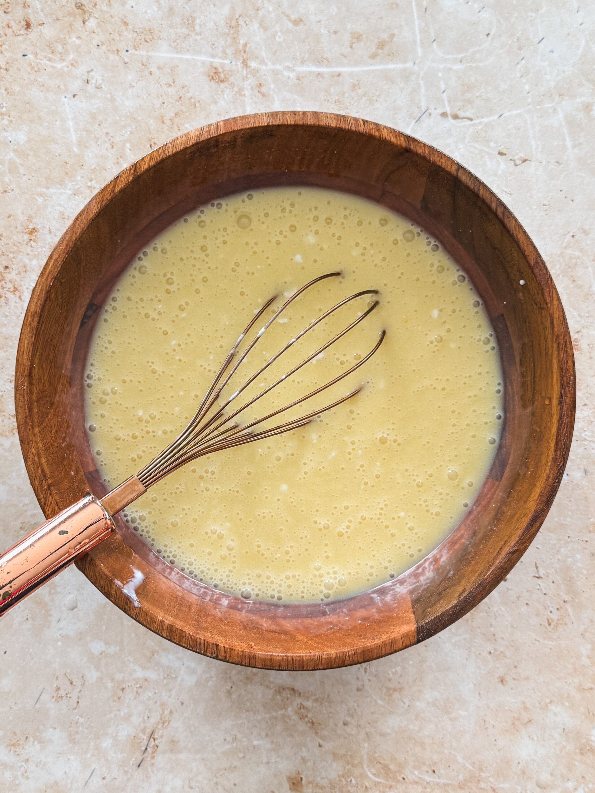 coconut milk mixed into wet ingredients in a wooden bowl