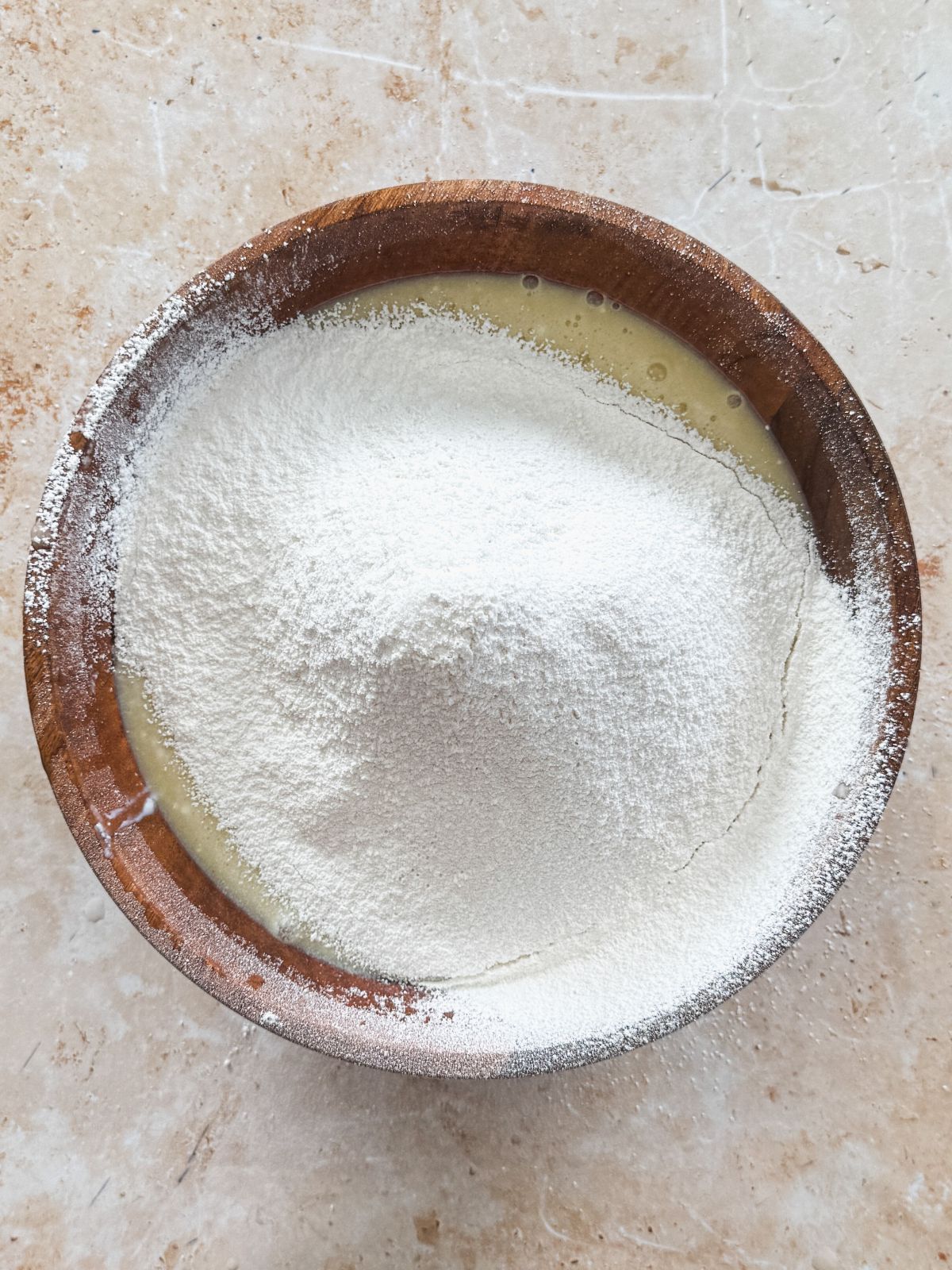 dry ingredients sifted on top of wet ingredients in a wooden bowl