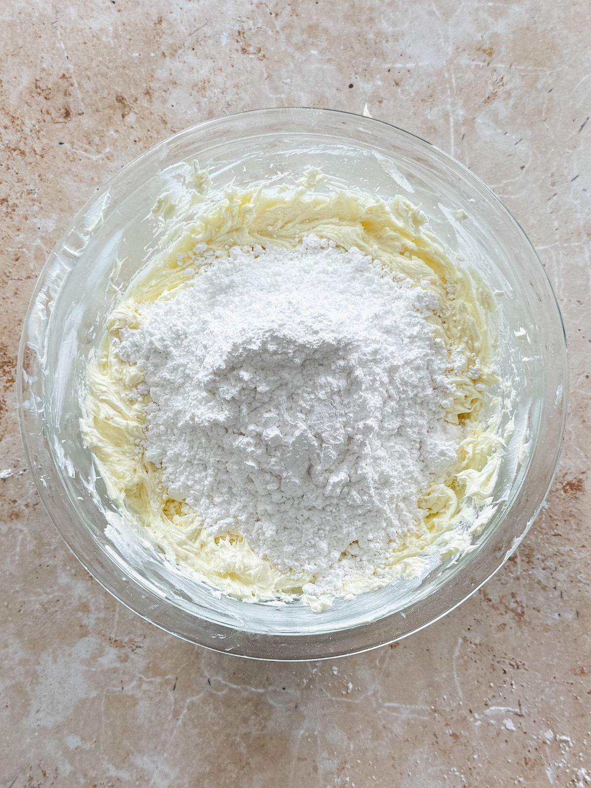 powdered sugar sifted on top of cream cheese in a glass bowl
