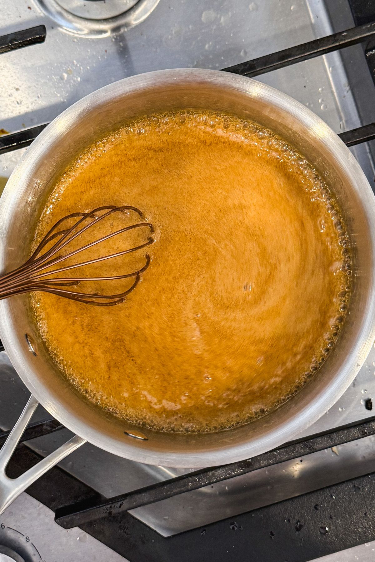 a hand whisking a maple sugar sauce in a stainless steel saucepan