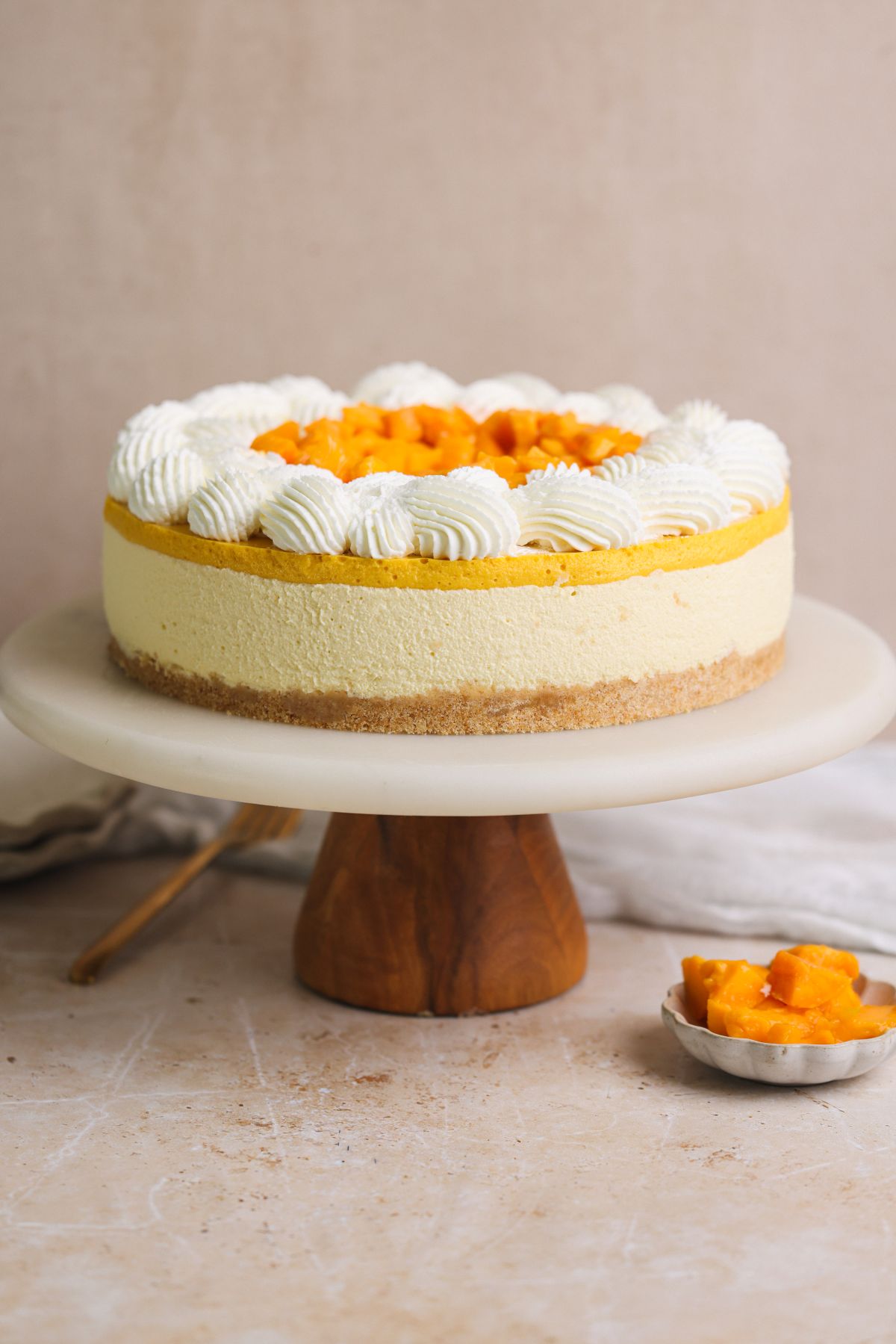 no bake mango cheesecake on a cake stand, decorated with whipped cream and fresh mangoes on top