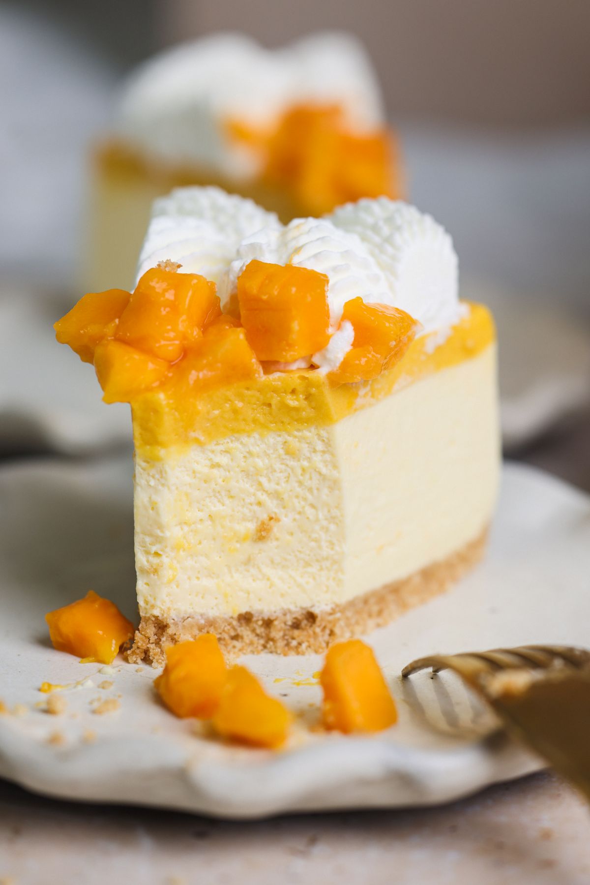 close up of a slice of mango cheesecake with a bite taken out to show the soft and creamy texture