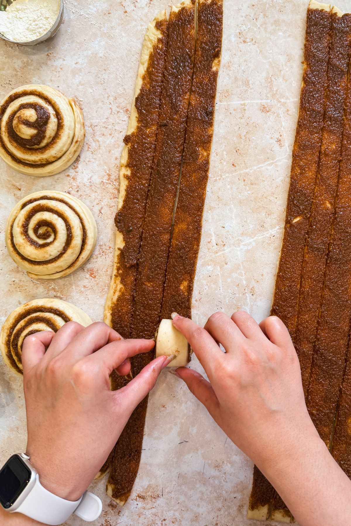 a hand rolling a strip of dough into a cinnamon roll