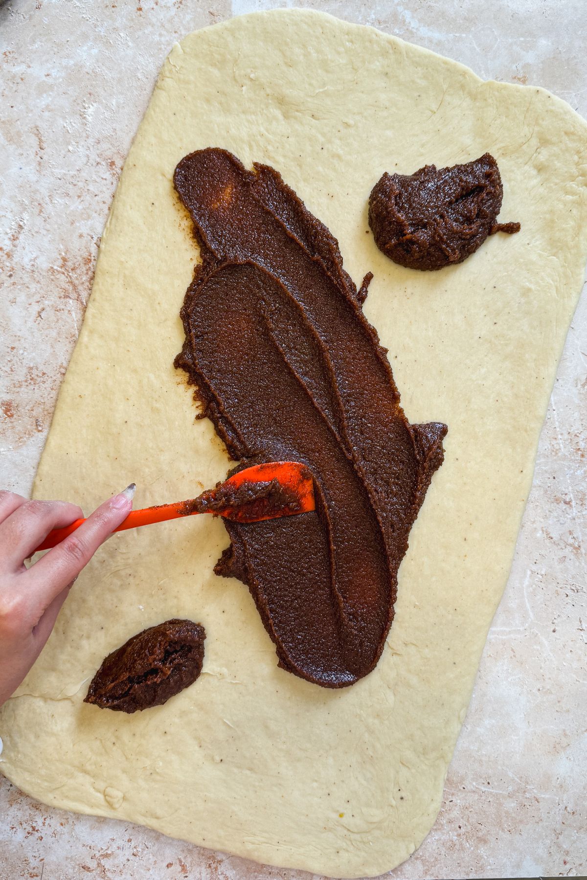 hand spreading a cinnamon sugar mixture on a rectangular sheet of dough