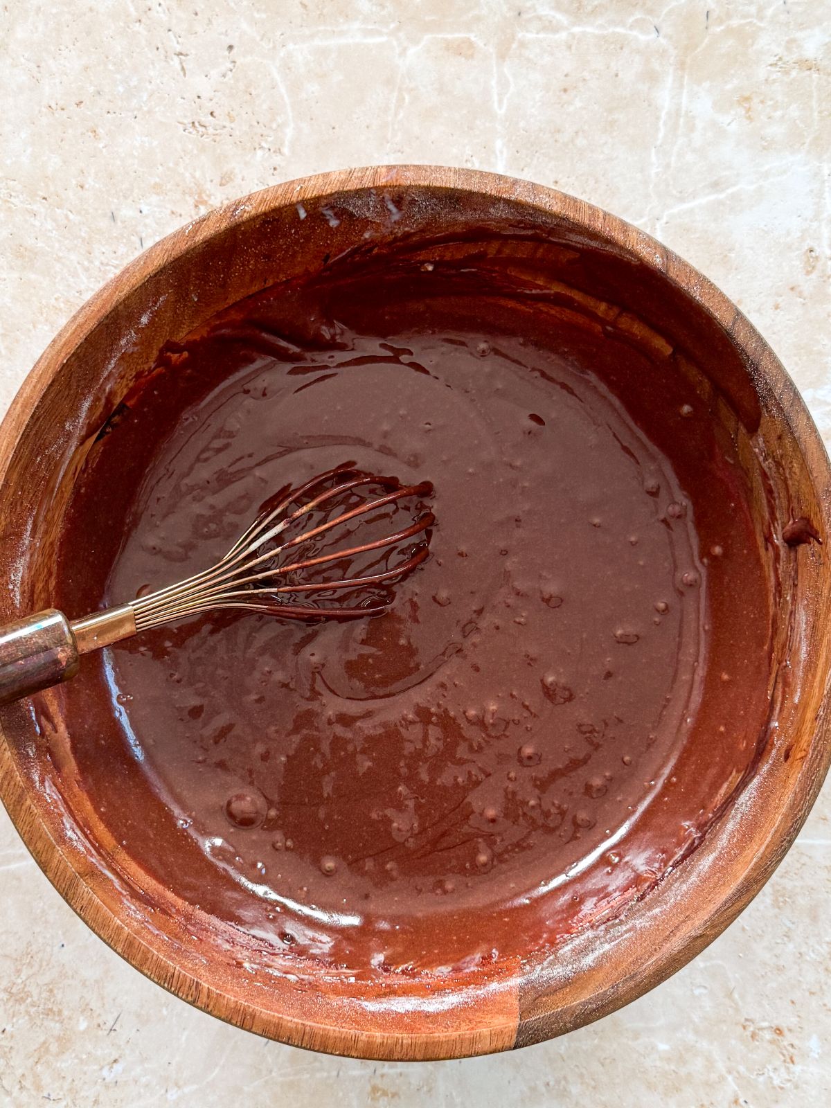 smooth and shiny chocolate cake batter in a wooden bowl with a whisk