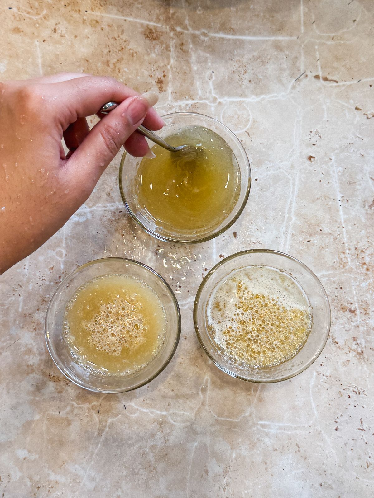 3 small bowls with bloomed gelatin with a hand dissolving the gelatin in one bowl