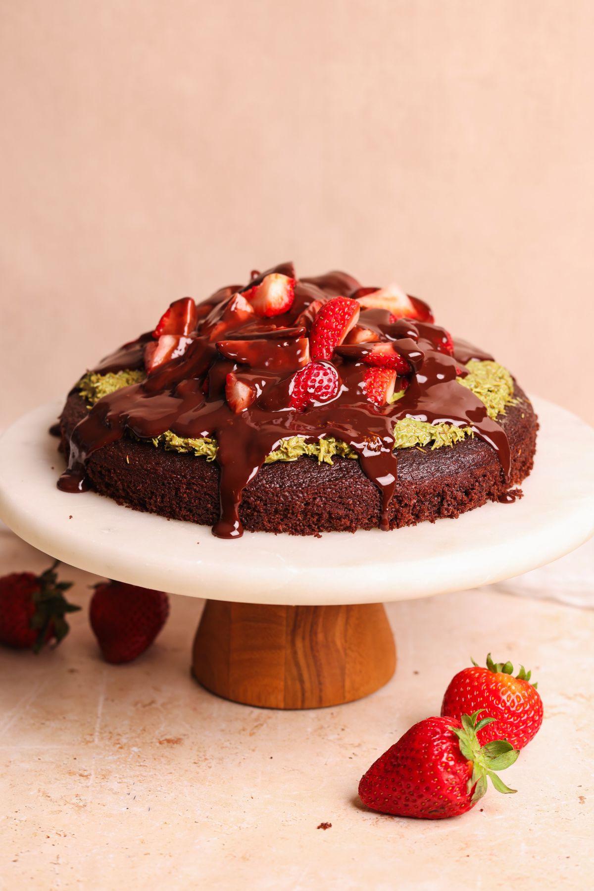 dubai chocolate strawberry cake on a cake stand. cake has pistachio knafeh, strawberries and chocolate ganache on top of it