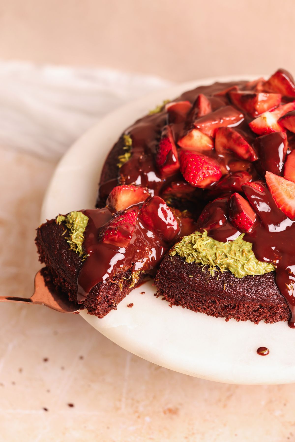 dubai chocolate strawberry cake on a cake stand with a spatula pulling out a slice